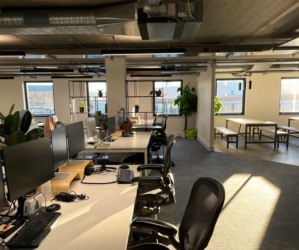 Open-plan shared office with desks, plants and a breakout area